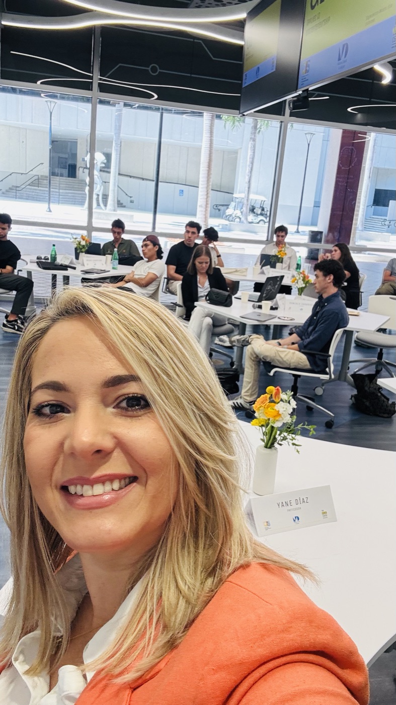 Yane at her professor desk at Miami Dade College with visiting university students from Spain behind her